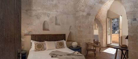 A bedroom with a wooden bed, a nightstand, a chair, and an arched stone ceiling.