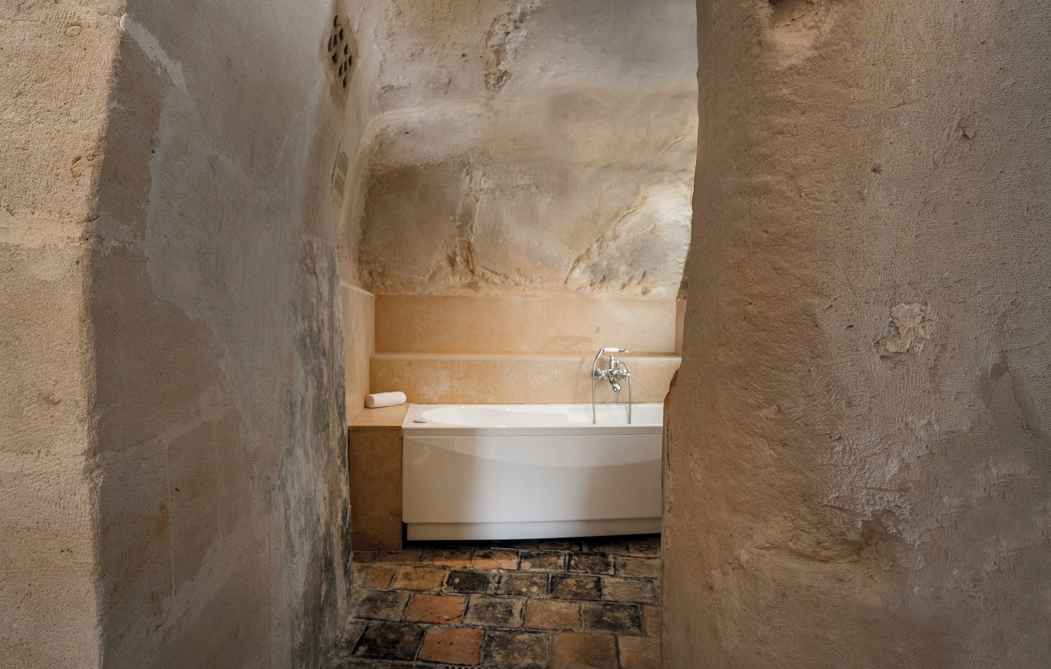 Un baño estrecho con paredes de piedra, una bañera blanca, una toalla y suelo de ladrillo.