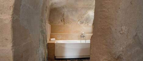 Un baño estrecho con paredes de piedra, una bañera blanca, una toalla y suelo de ladrillo.