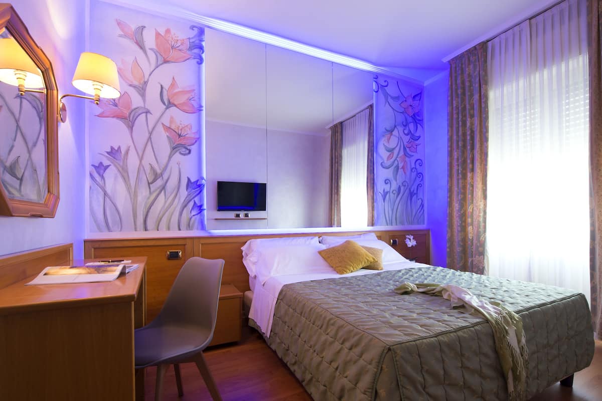 A hotel room with a bed, desk, chair, and a television.
