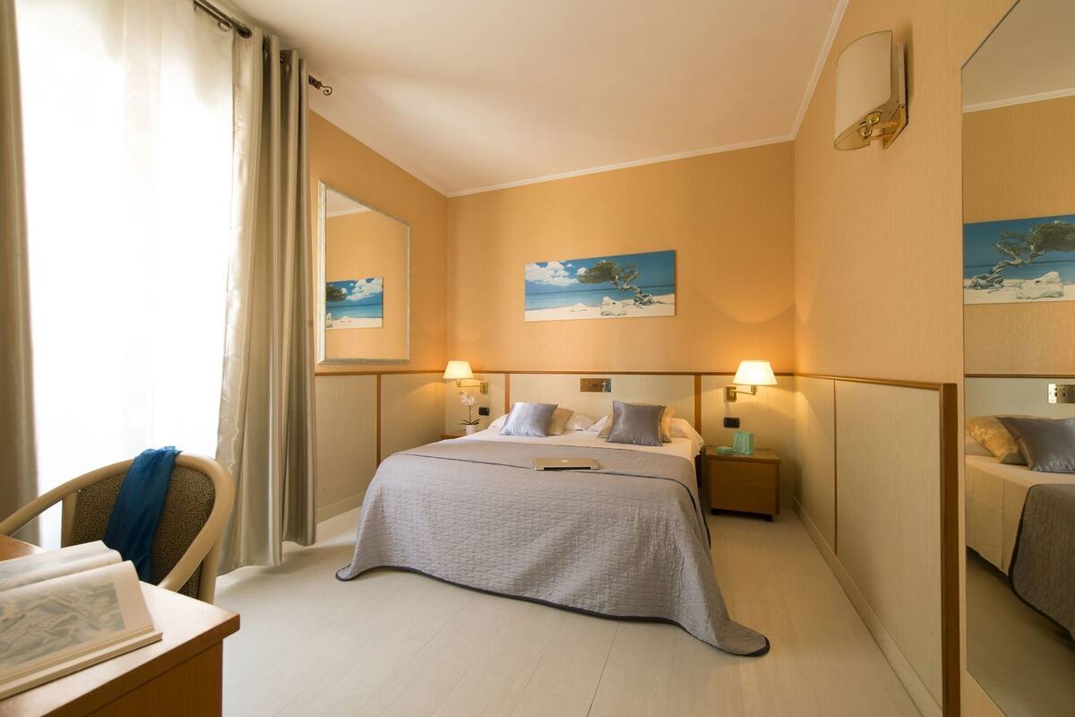A hotel room with a bed, two bedside tables, a desk, and a chair.