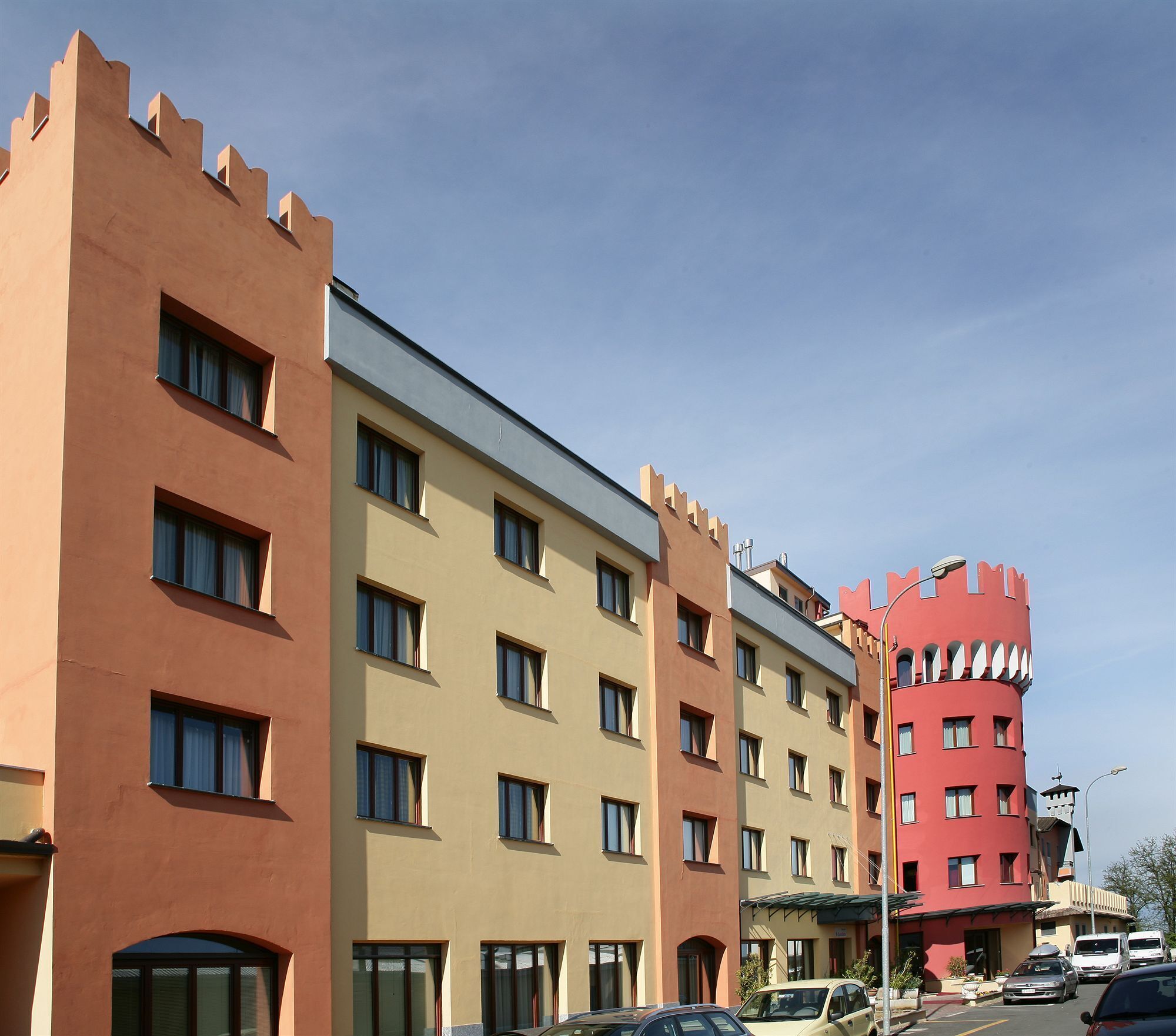Un hotel a più piani con facciata simile a un castello, ampie finestre e un parcheggio con automobili.