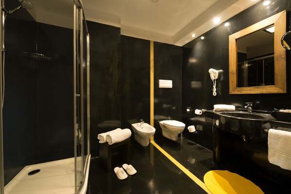 A modern bathroom with a black and yellow color scheme, including a shower, bidet, toilet, sink, and a mirror. - Hotel Il Castelletto (Casarile)