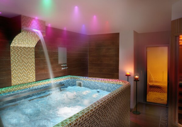 A modern spa with a tiled hot tub, a water feature, and ambient lighting. - Hotel Il Castelletto (Casarile)
