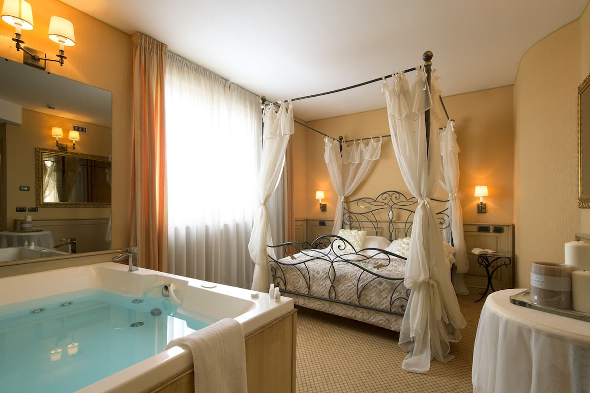 A hotel room with a four-poster bed, a large bathtub, and a separate vanity with a mirror.