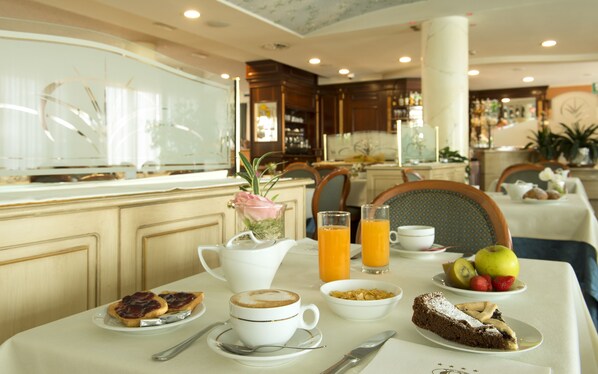 A breakfast setting with a table set for two, including a coffee cup, orange juice, toast, cereal, fruit, and a slice of cake. - Hotel Il Castelletto (Casarile)