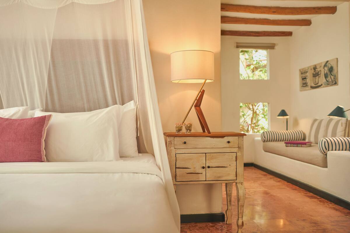 Un dormitorio con cama, mesita de noche, lámpara y un sofá.