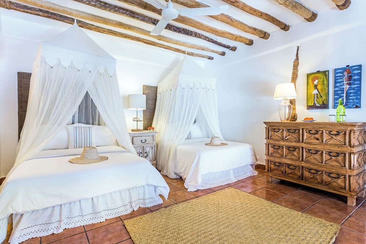 A bedroom with two beds, a wooden dresser, and a ceiling fan.