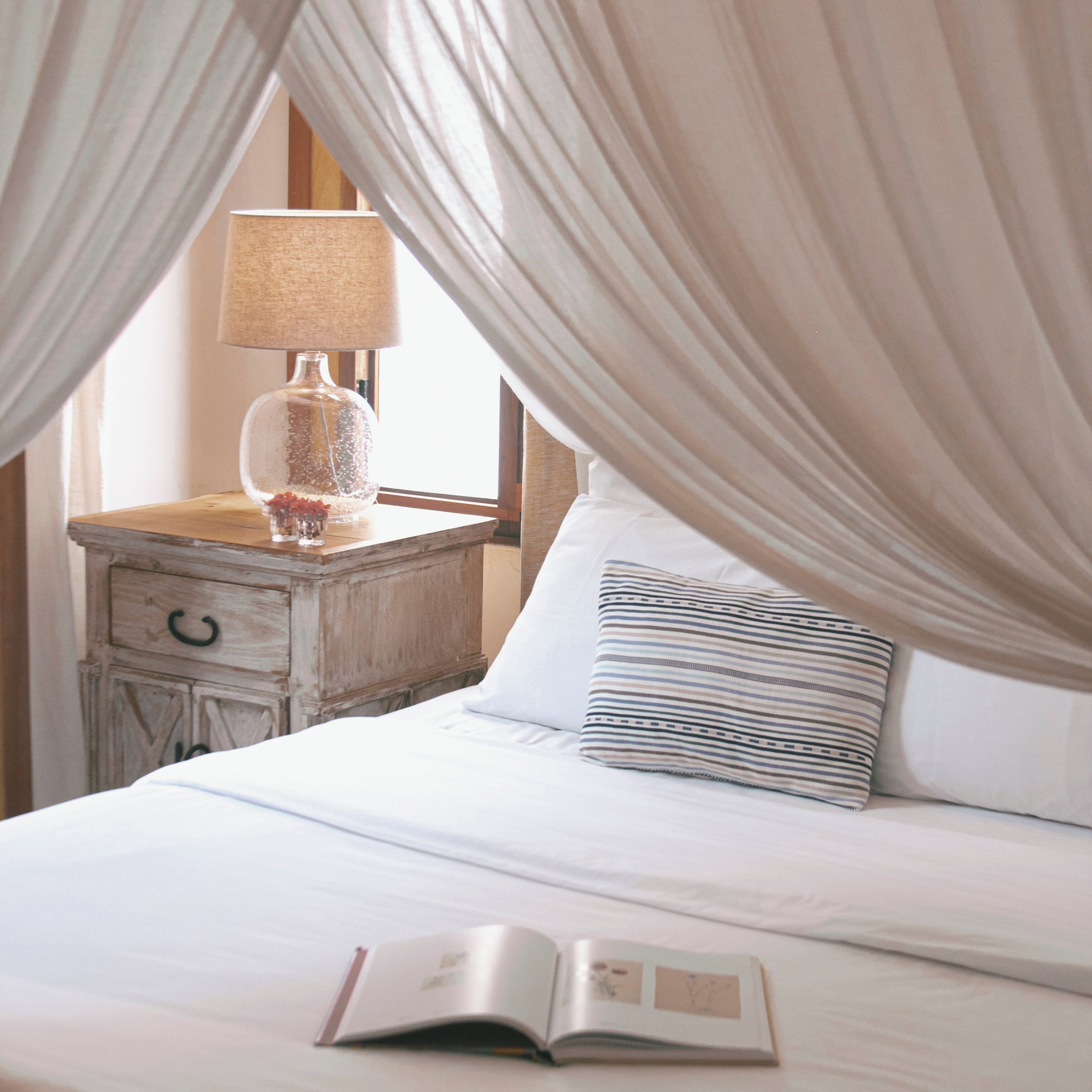 A bed with a canopy, a bedside table with a lamp, and an open book on the bed.