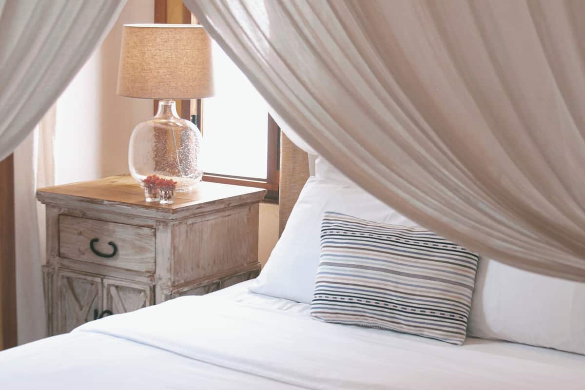 Una cama con dosel, una mesita de noche con lámpara y un libro abierto sobre la cama.
