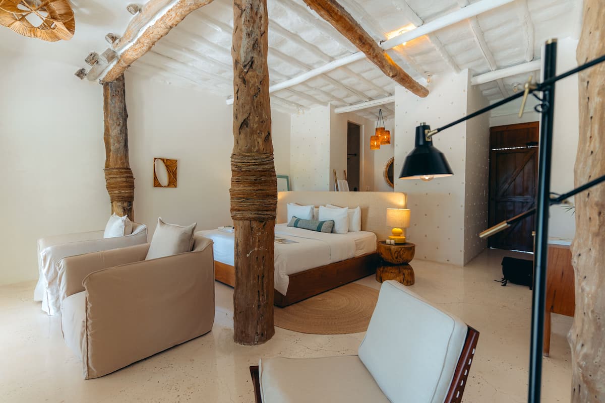 Una habitación con una cama, dos sofás, un pilar de madera, una lámpara y un espejo en la pared.