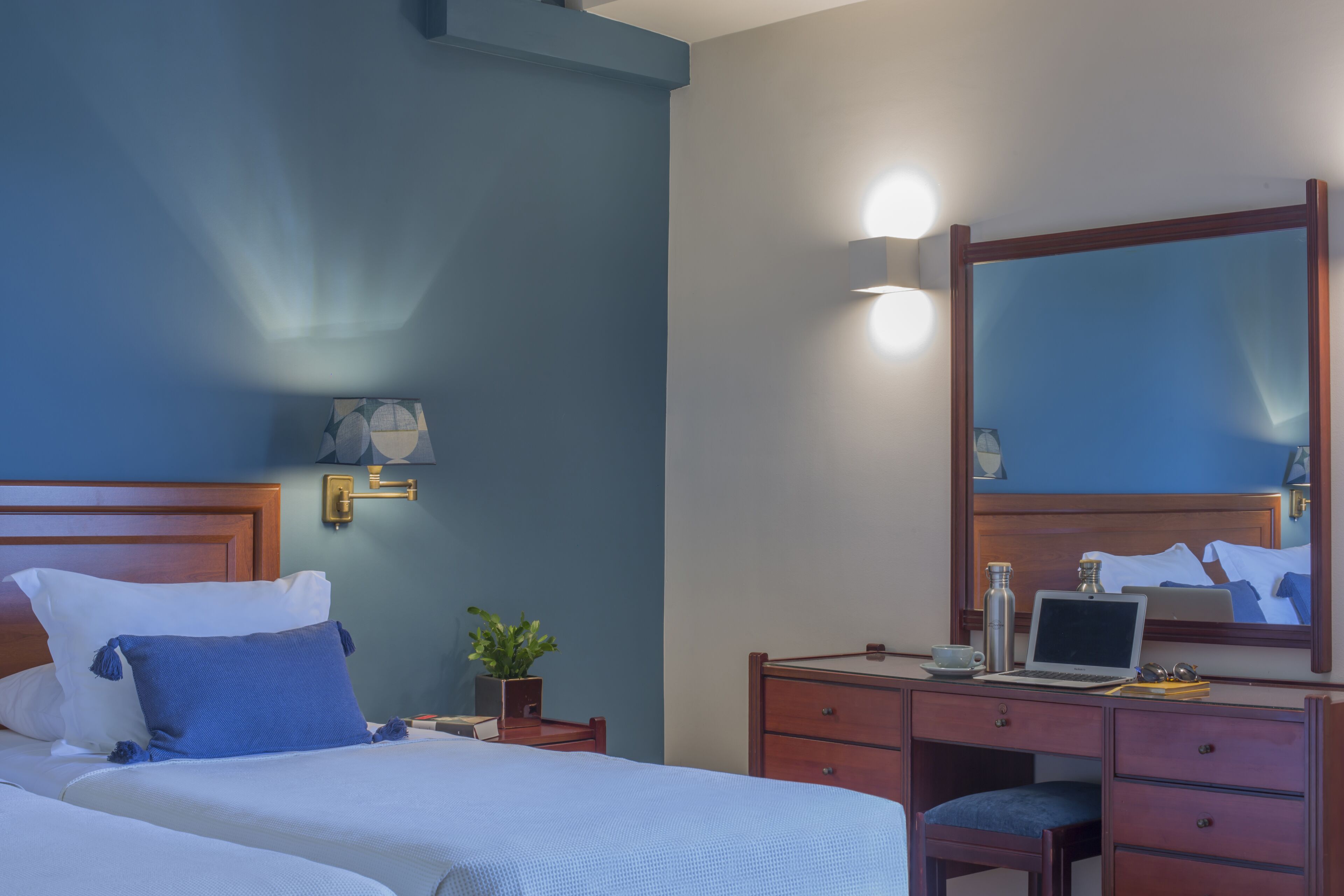 Habitación de hotel con una cama, un escritorio, una silla, una computadora portátil y un espejo.