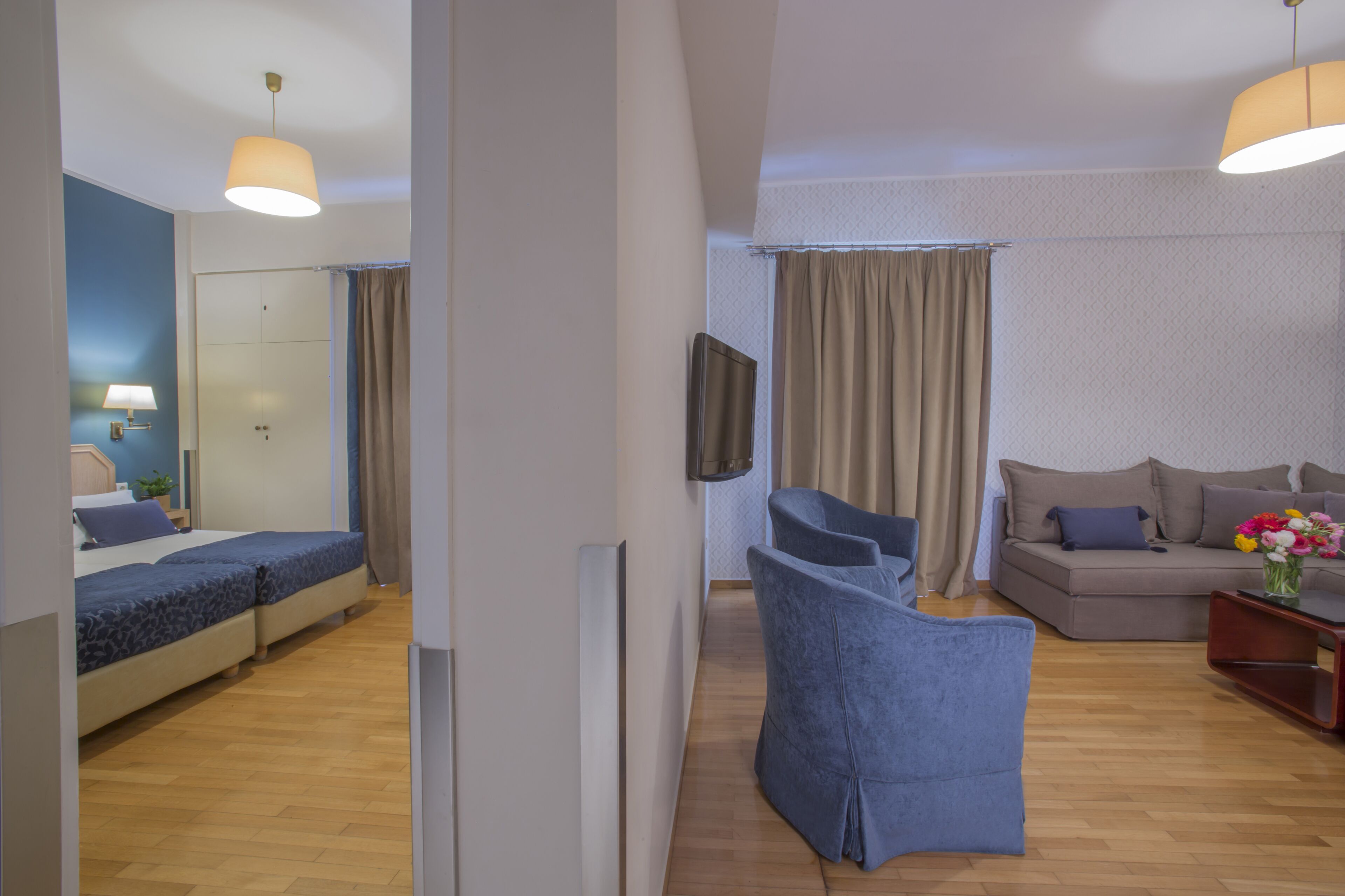 A modern hotel room with a bed, a sofa, a TV, and a small table with a vase of flowers.