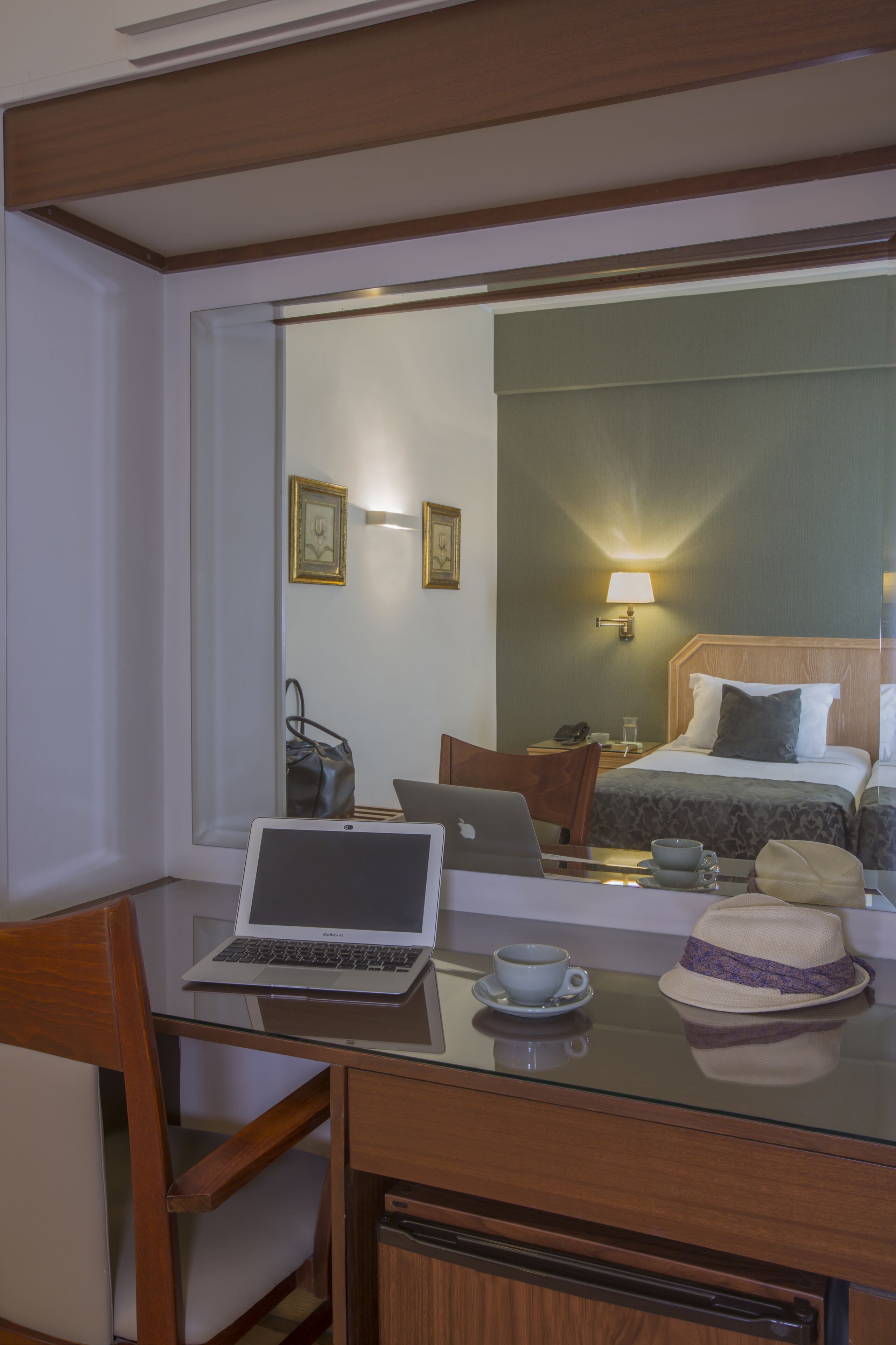 A hotel room with a desk, laptop, chair, and a bed with a headboard.