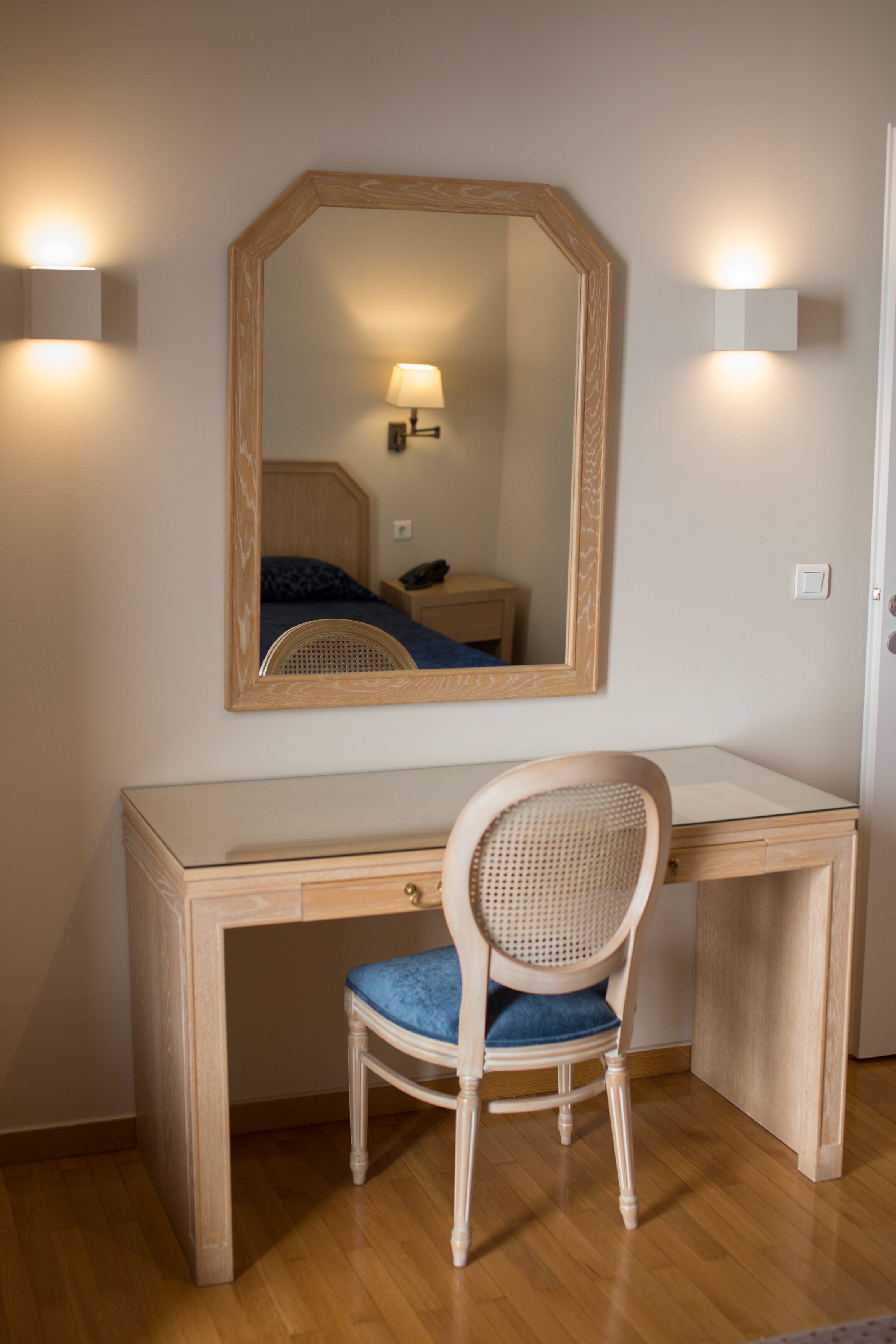 A wooden desk with a chair, a mirror, and bedside lamps.