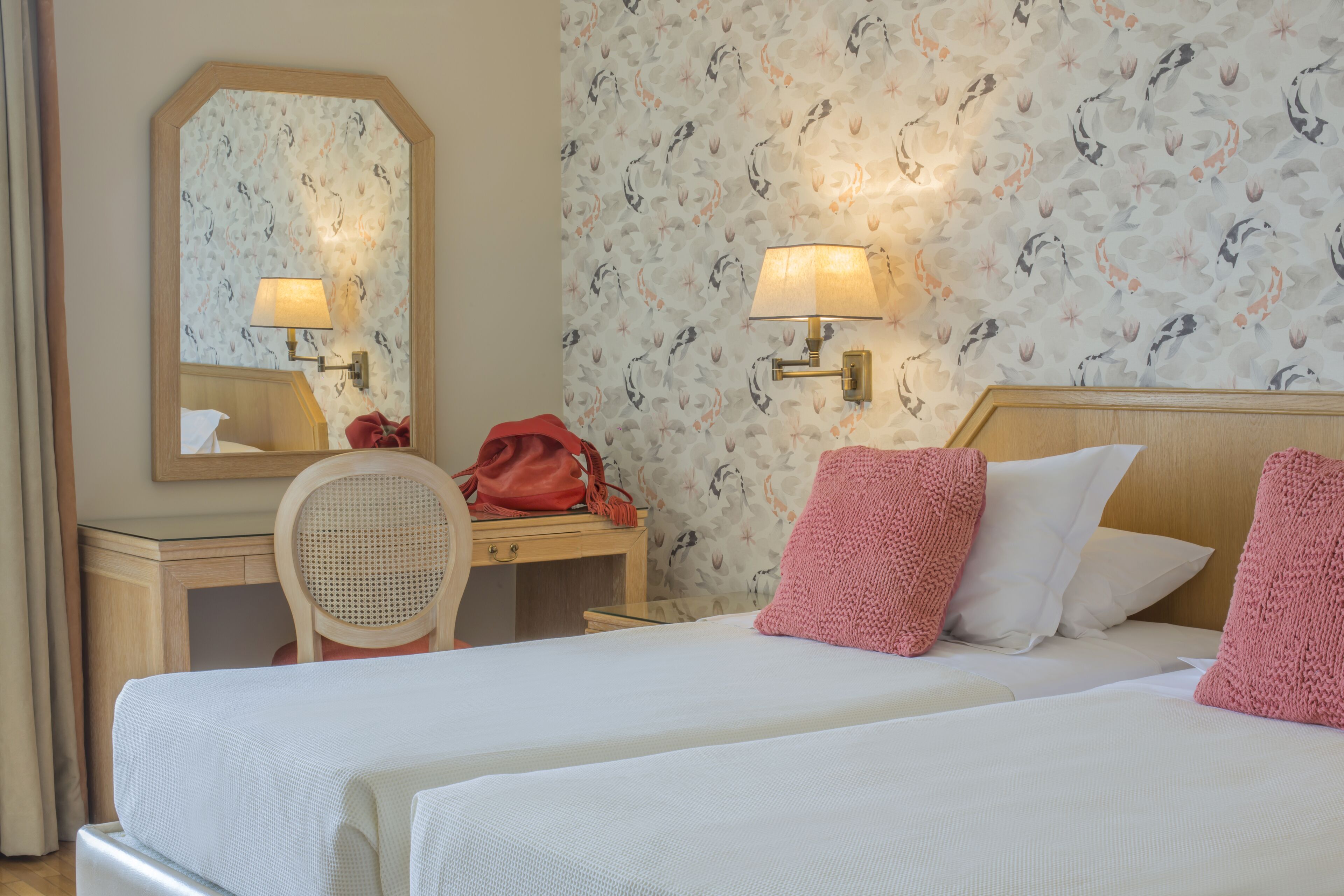 Une chambre d’hôtel avec deux lits, un bureau en bois, une chaise, un miroir et deux lampes fixées au mur.