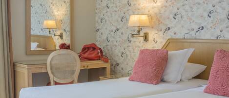 Une chambre d’hôtel avec deux lits, un bureau en bois, une chaise, un miroir et deux lampes fixées au mur.