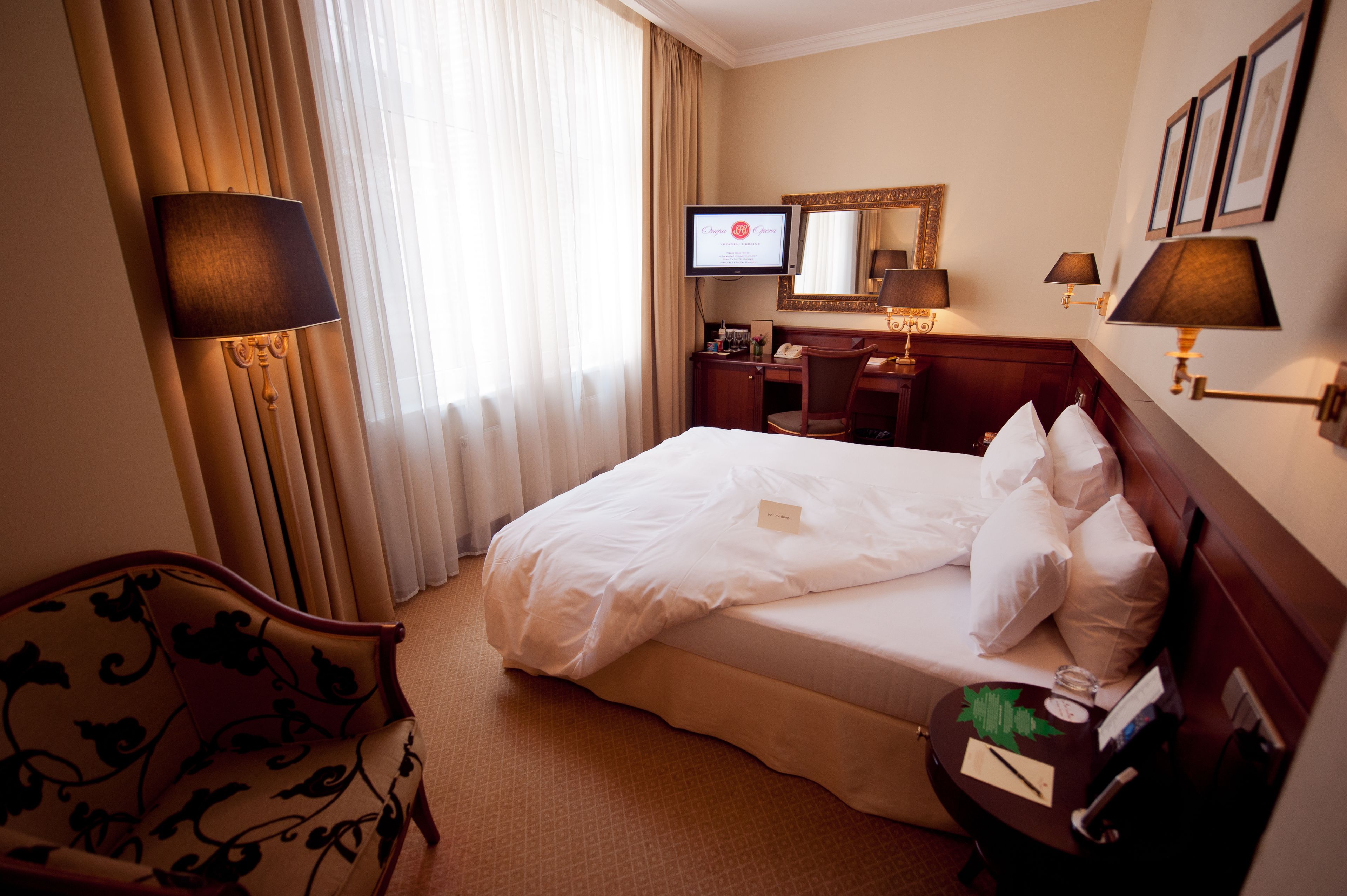 A hotel room with a large bed, a desk, a chair, a TV, and a mirror.