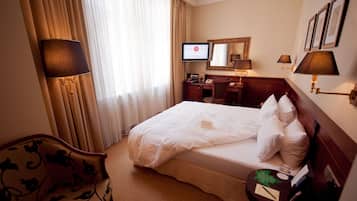 A hotel room with a large bed, a desk, a chair, a TV, and a mirror.