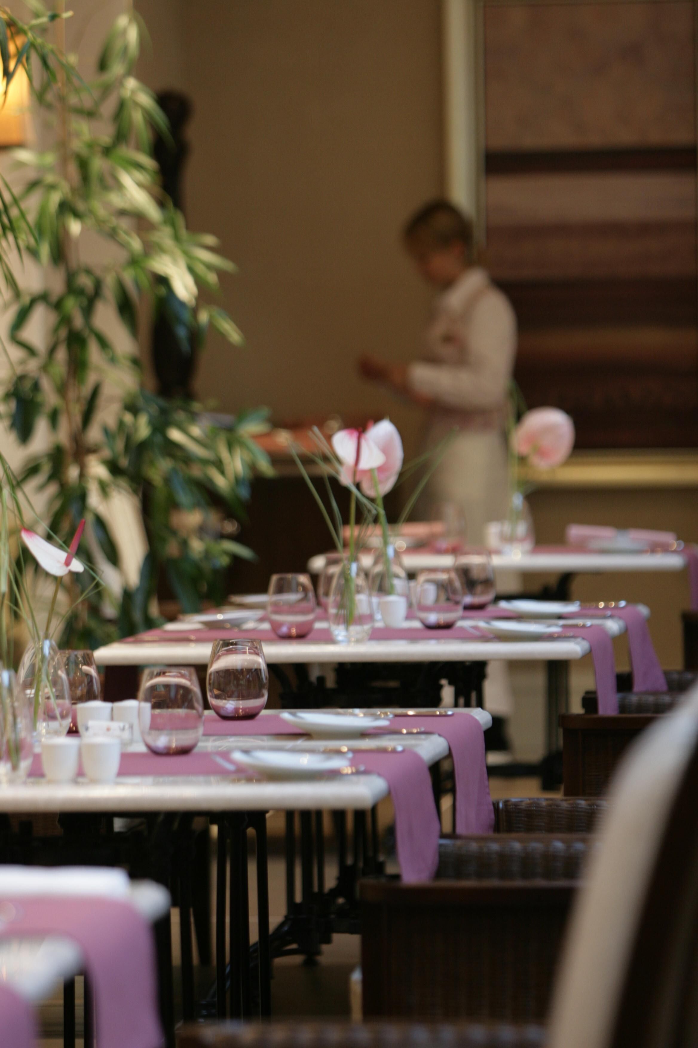 Un restaurante con mesas dispuestas para comer, con manteles rosas y cristalería.