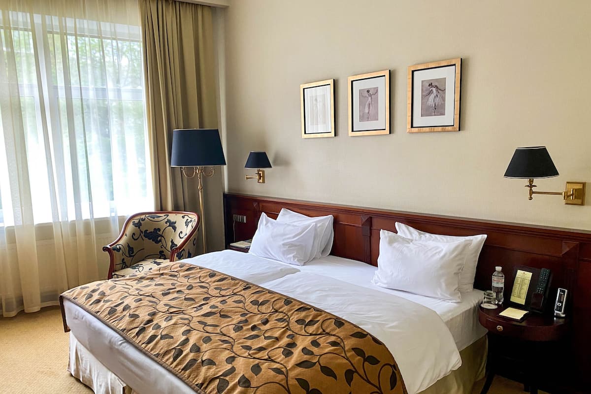 Habitación de hotel con una cama grande, una silla, una mesita de noche y tres cuadros en la pared.