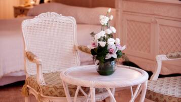 Een klassieke kamer met een bed, twee stoelen, een ronde tafel met een bloemenvaas en twee lampen op nachtkastjes.