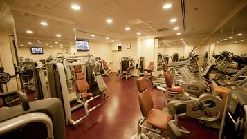 A gym with various exercise machines, a television, and a mirror on the wall.