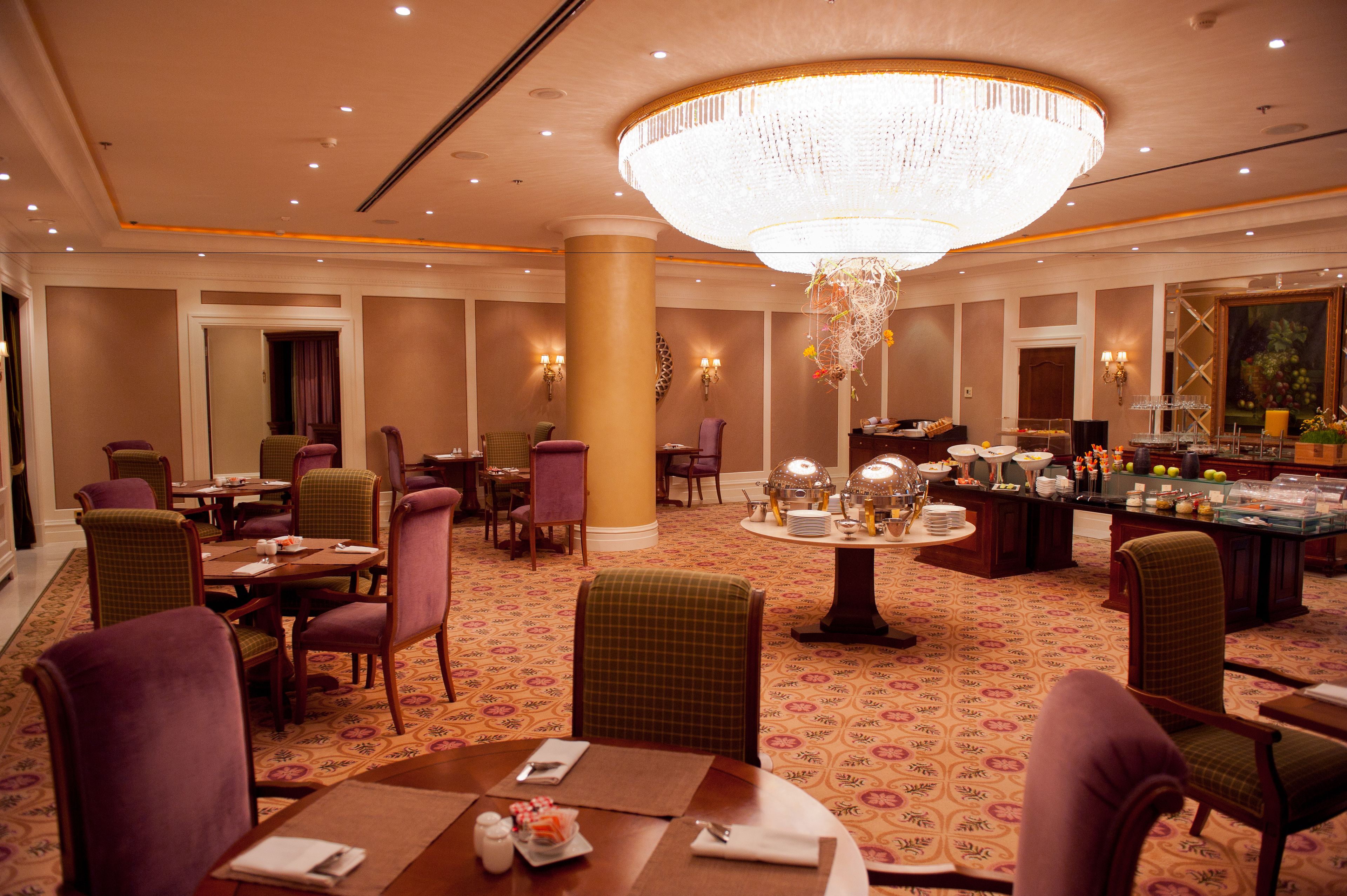 A hotel lobby with multiple dining tables, chairs, a large chandelier, and a bar area.