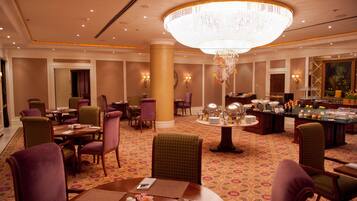 A hotel lobby with multiple dining tables, chairs, a large chandelier, and a bar area.