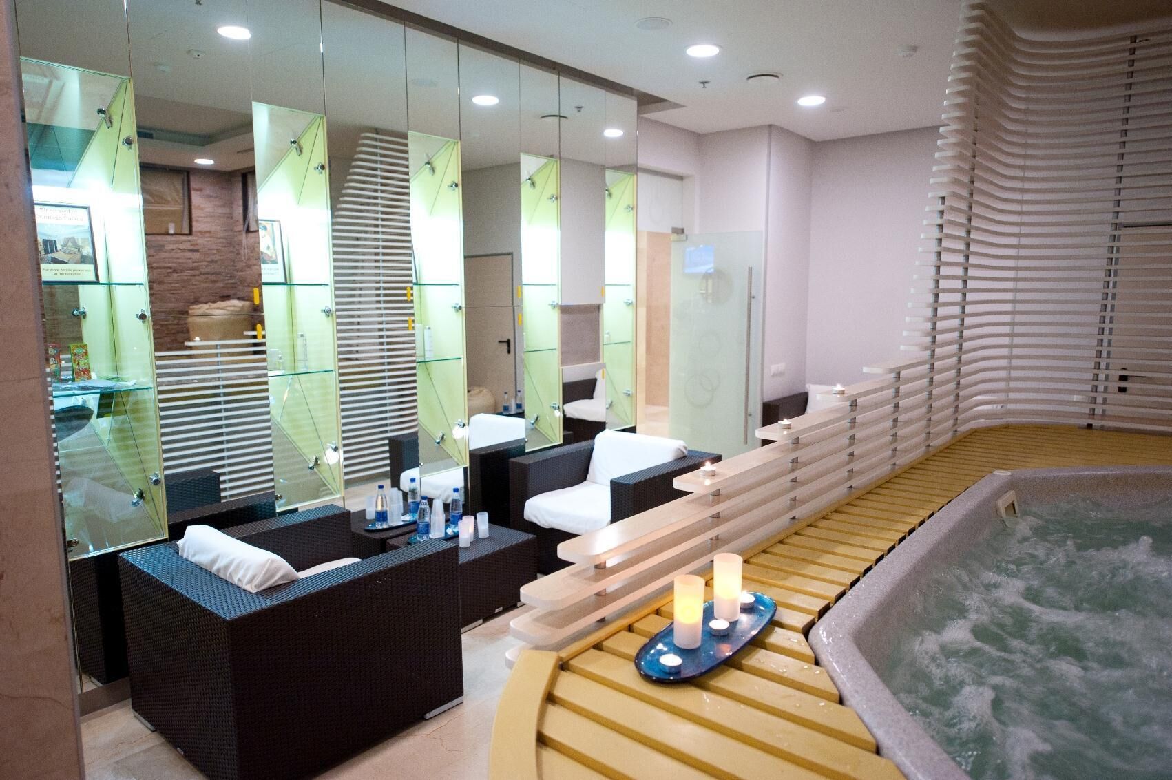 A modern spa area with a large bathtub, a seating area with a massage table, and a counter with a sink and mirrors.