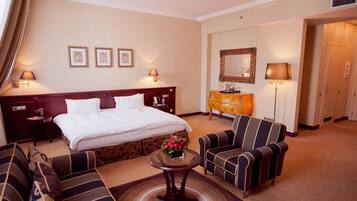 A hotel room with a large bed, two bedside tables, a dresser, a sofa, and a small table with a vase of flowers.