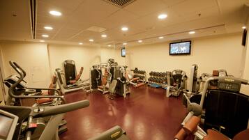 A gym with various exercise machines, a television screen, and dumbbells.