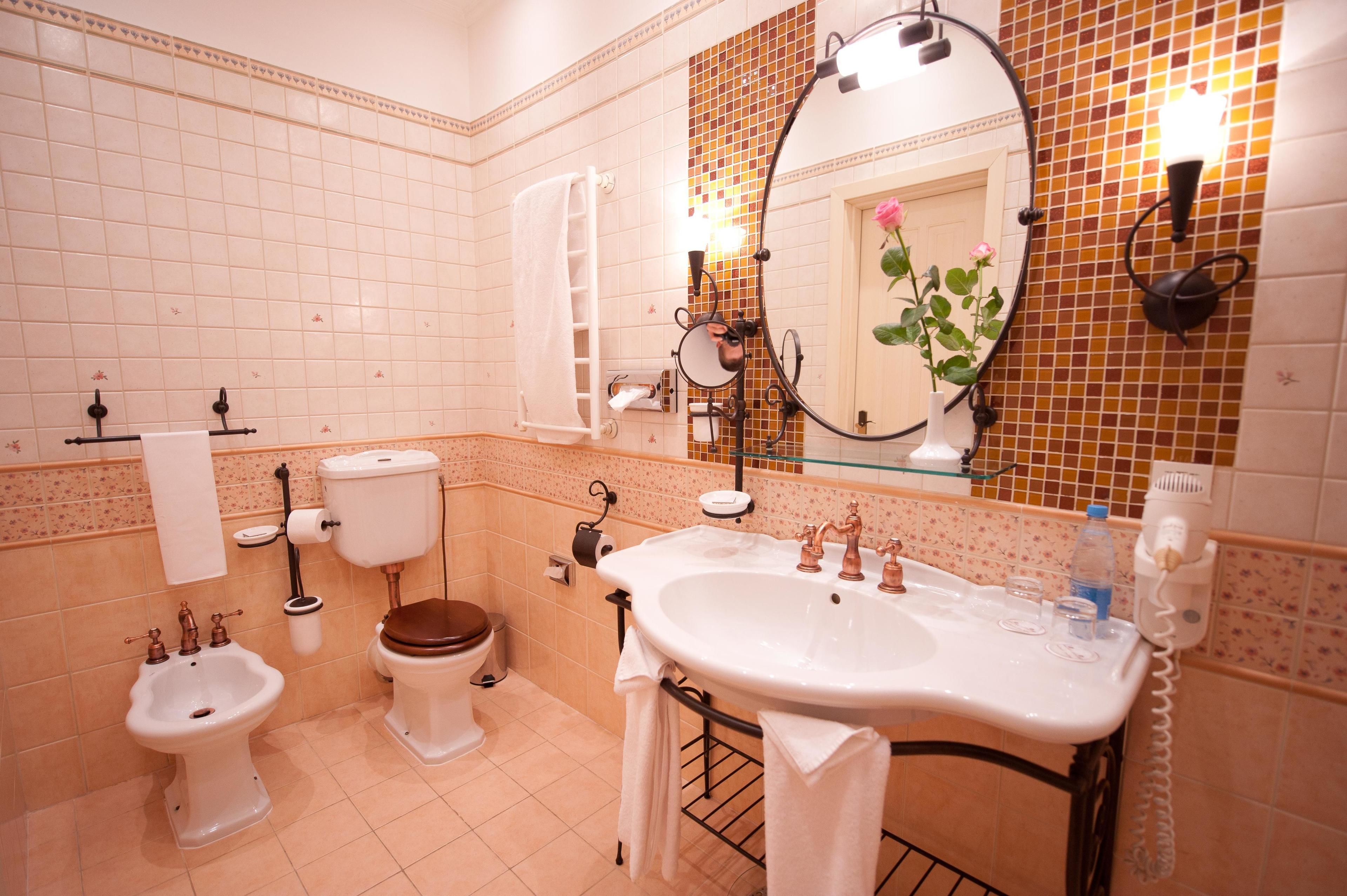 Een badkamer met toilet, bidet, wastafel en een spiegel met bloemdecoratie.