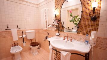 Een badkamer met toilet, bidet, wastafel en een spiegel met bloemdecoratie.