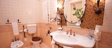 A bathroom with a toilet, bidet, sink, and a mirror with a flower decoration.
