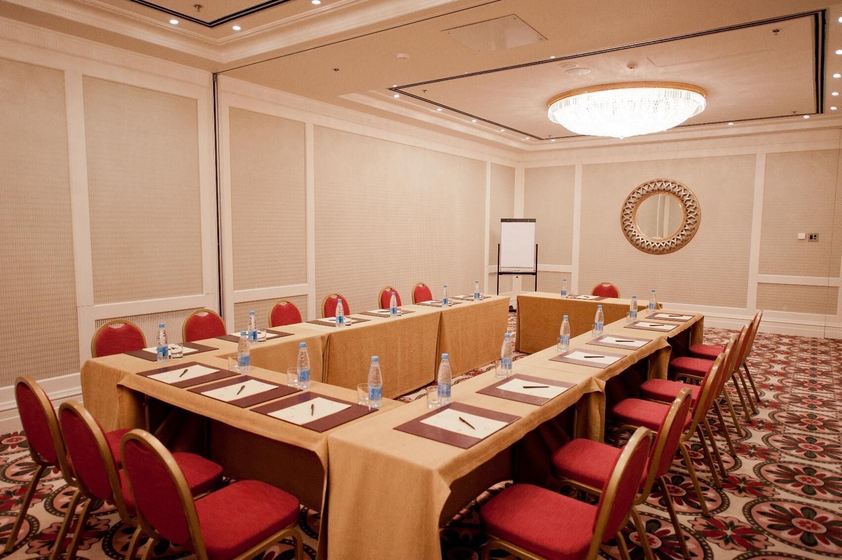 A conference room with a long table, red chairs, water bottles, and a whiteboard.