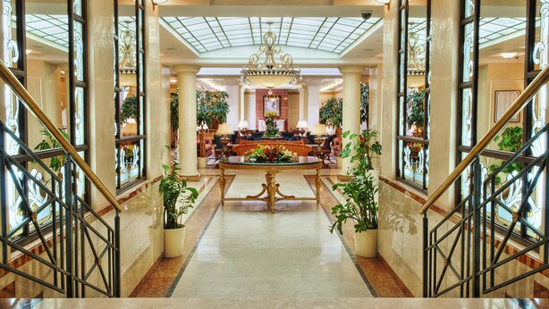 Un vaste hall d’entrée avec un espace salon central, de grandes fenêtres et des plantes en pot.