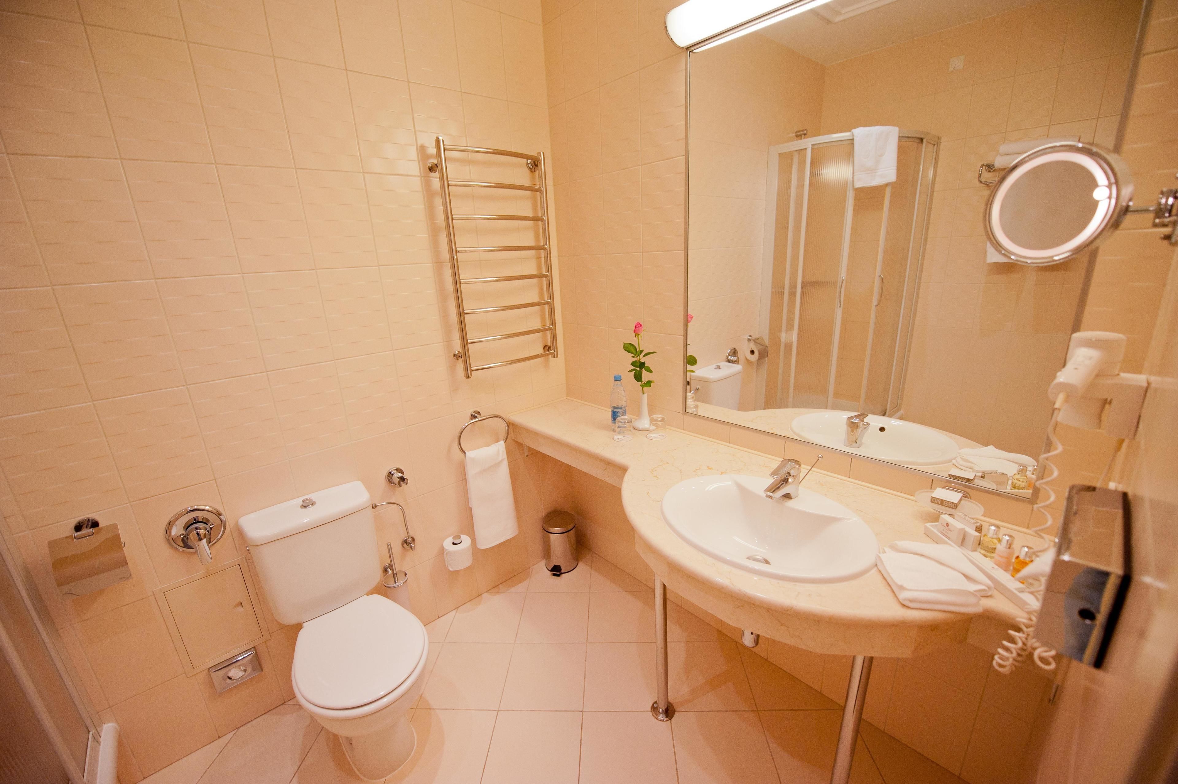 A bathroom with a toilet, sink, mirror, towel rack, and a trash bin.