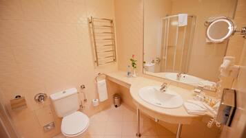 A bathroom with a toilet, sink, mirror, towel rack, and a trash bin.