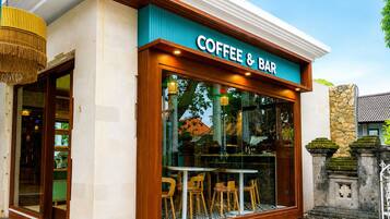 A coffee and bar with a large window, wooden exterior, and a stone wall with a cross.