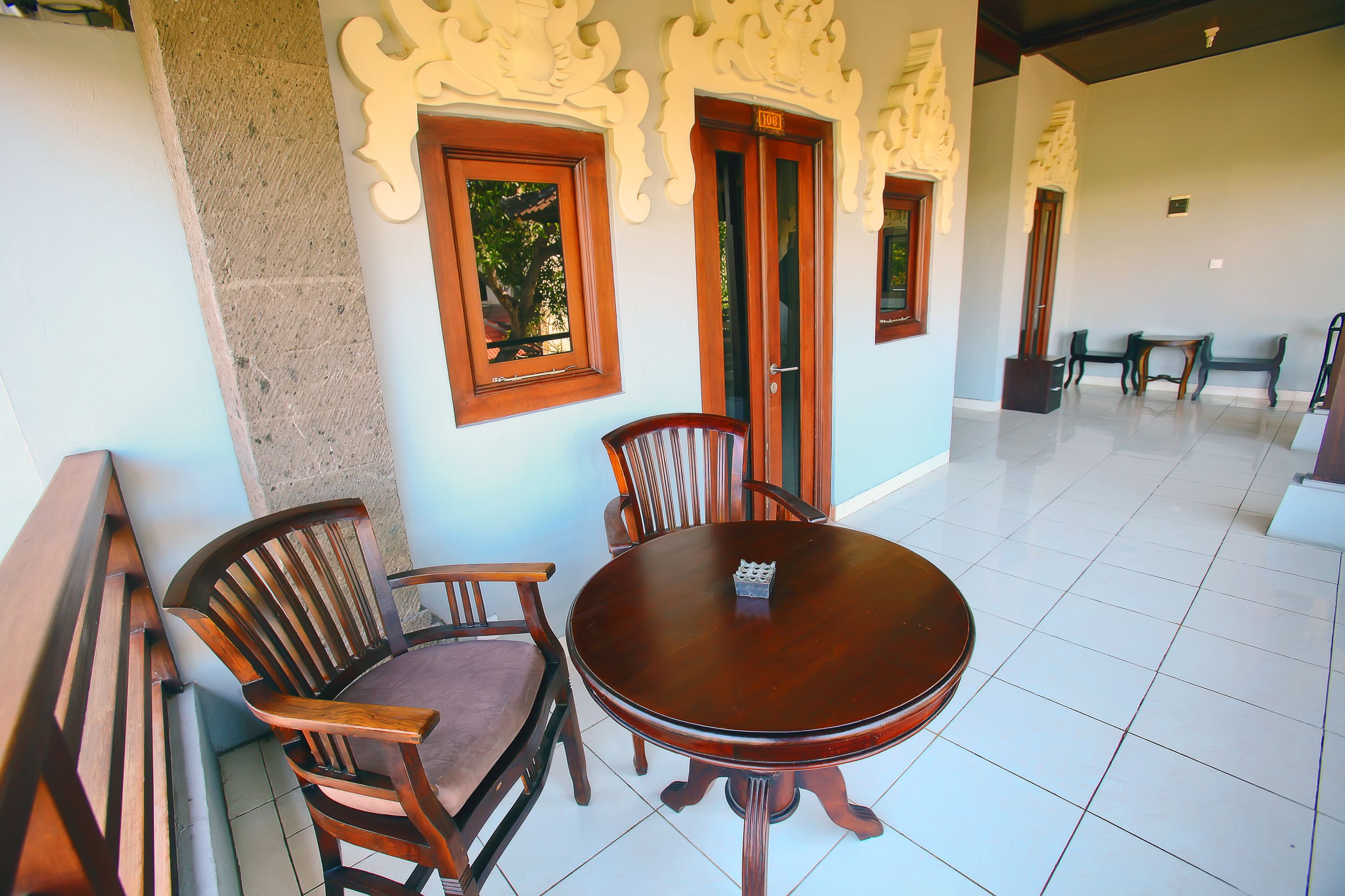 Un comedor con una mesa redonda de madera y sillas, decoraciones ornamentales en la pared y suelo de baldosas.