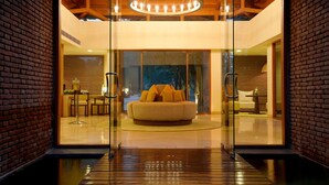A modern interior with a glass door leading to a living area featuring a sofa and a dining table. - The Westin Sohna Resort & Spa (Sohna)