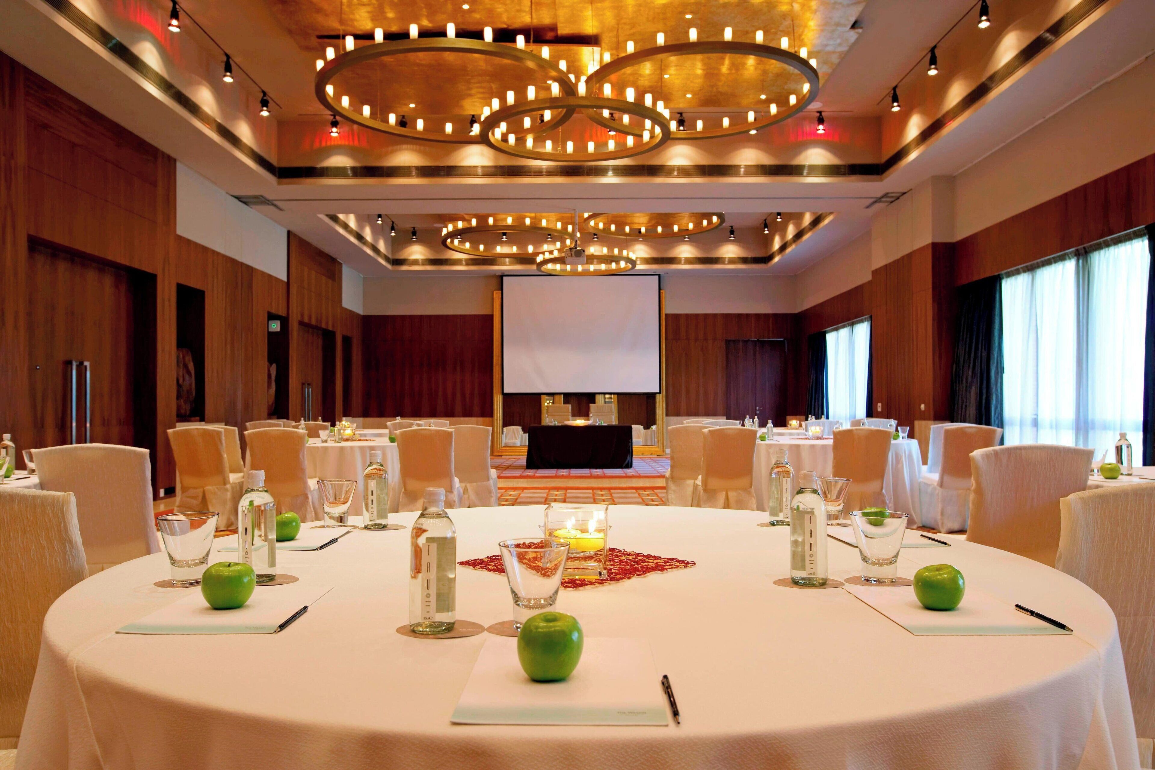 A conference room with round tables, chairs, and a large screen at the front.