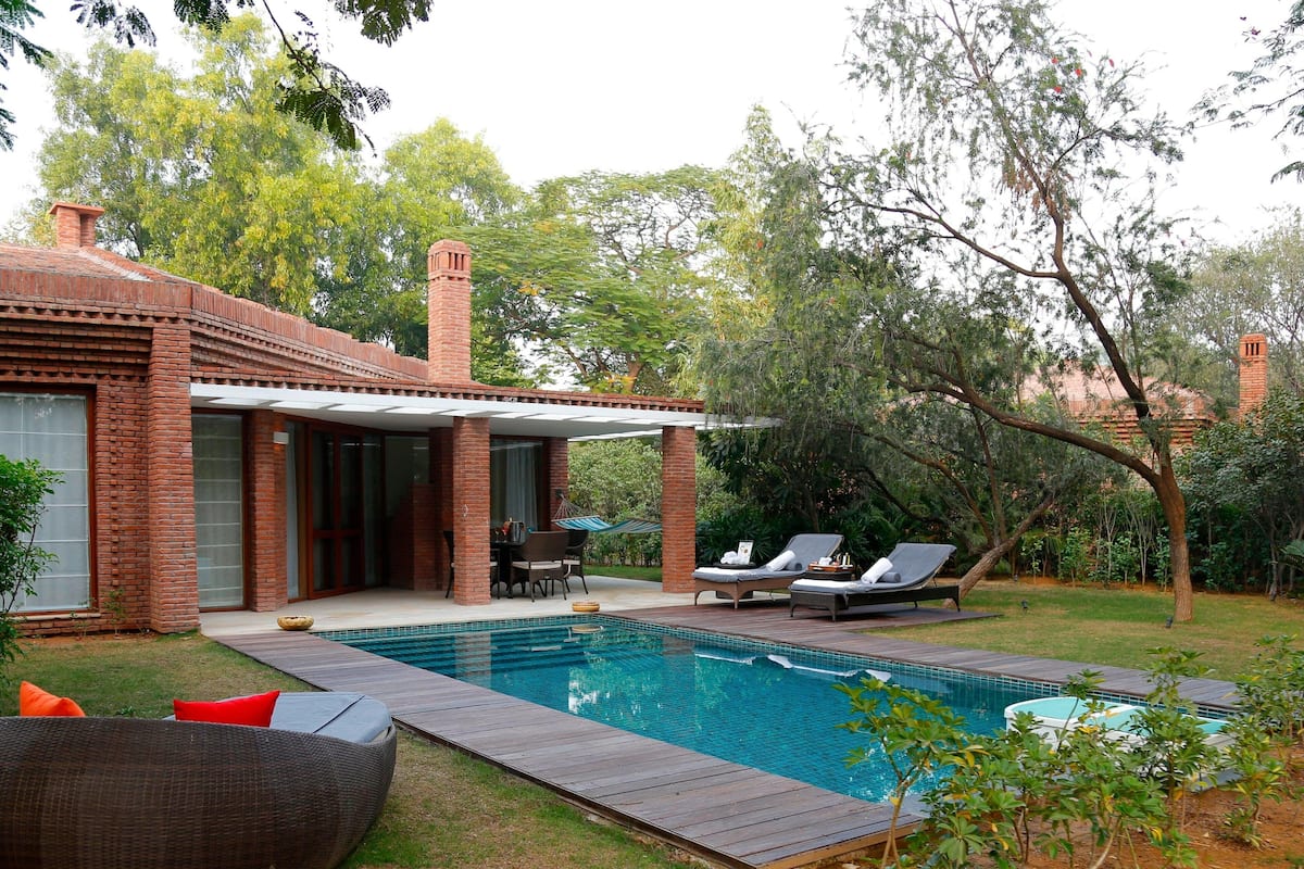 A poolside area with a brick house, a covered patio, and lounge chairs.