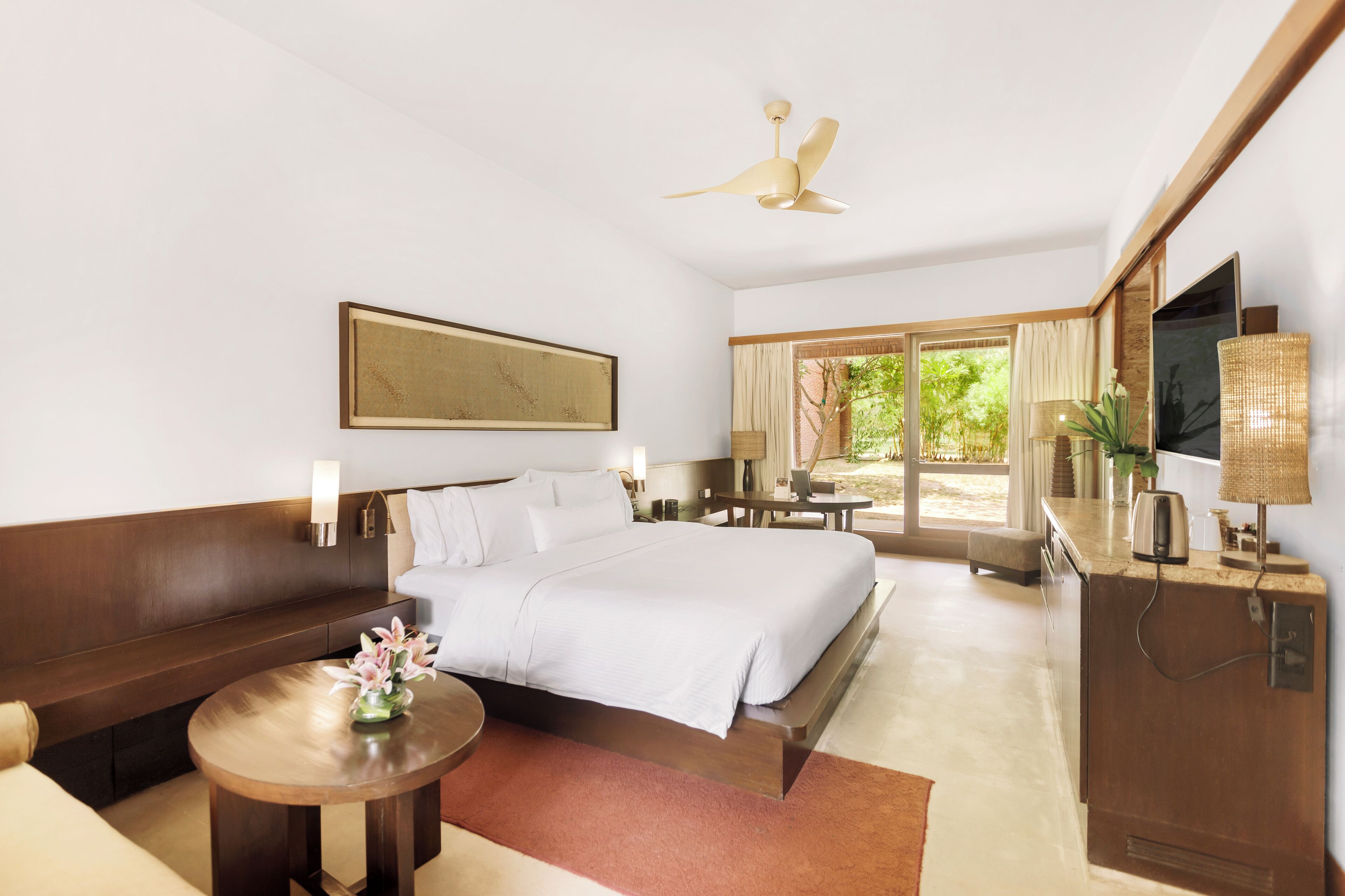 Habitación de hotel con cama, sofá, escritorio, televisor y ventana con vistas a zonas verdes.