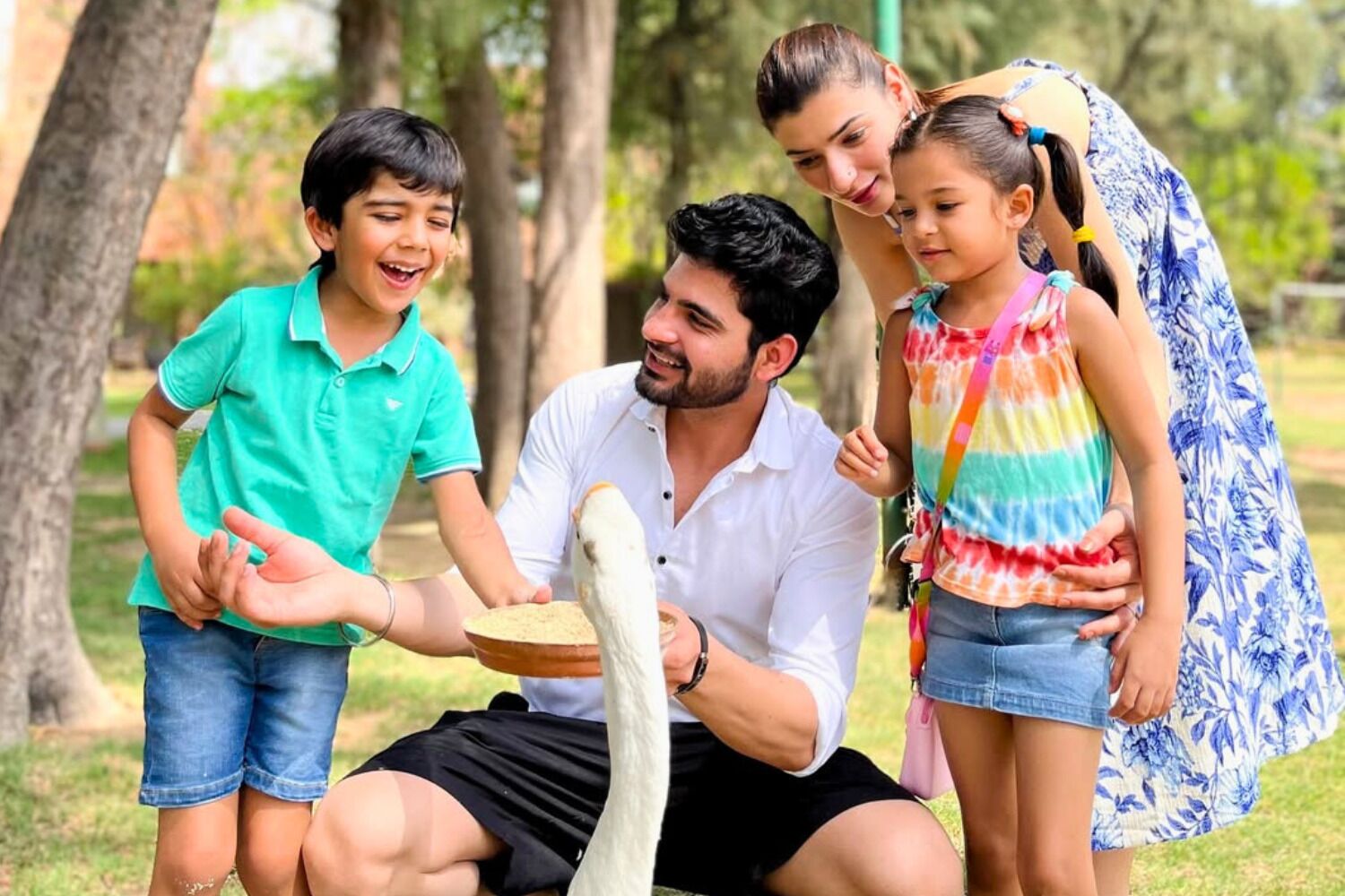 Une famille, dont un enfant, nourrit un grand oiseau dans un parc.
