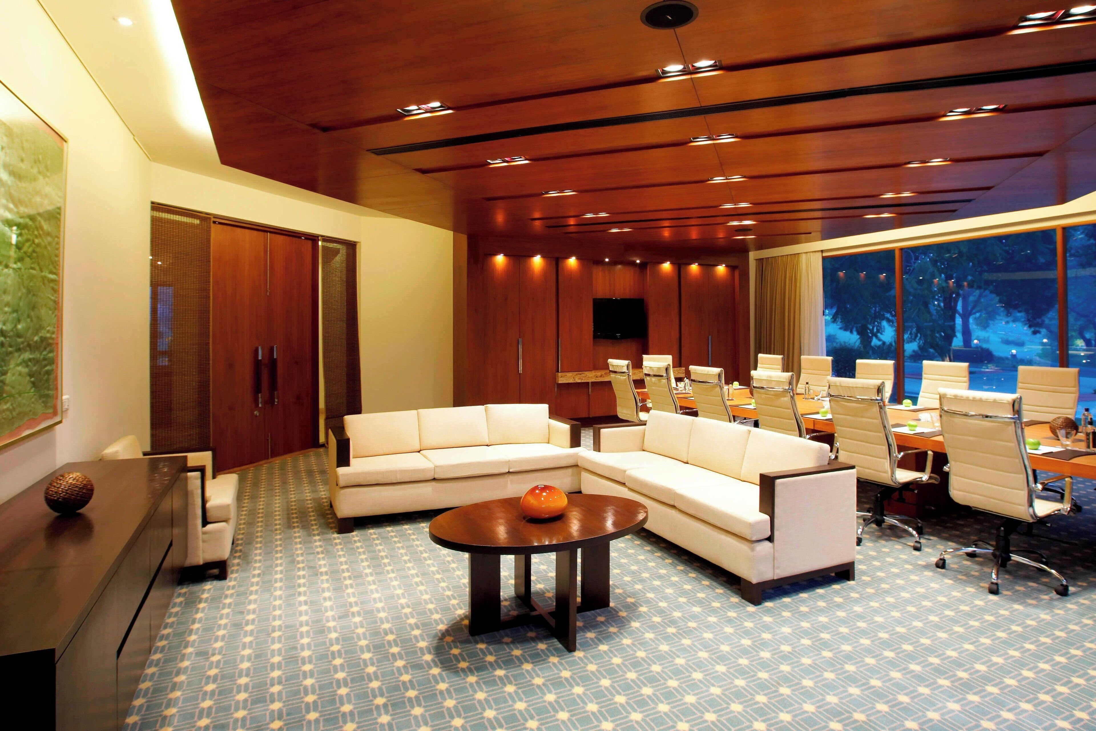 Een moderne hotellobby met een ruim zithoek, een vergaderruimte en een groot raam met uitzicht op bomen.