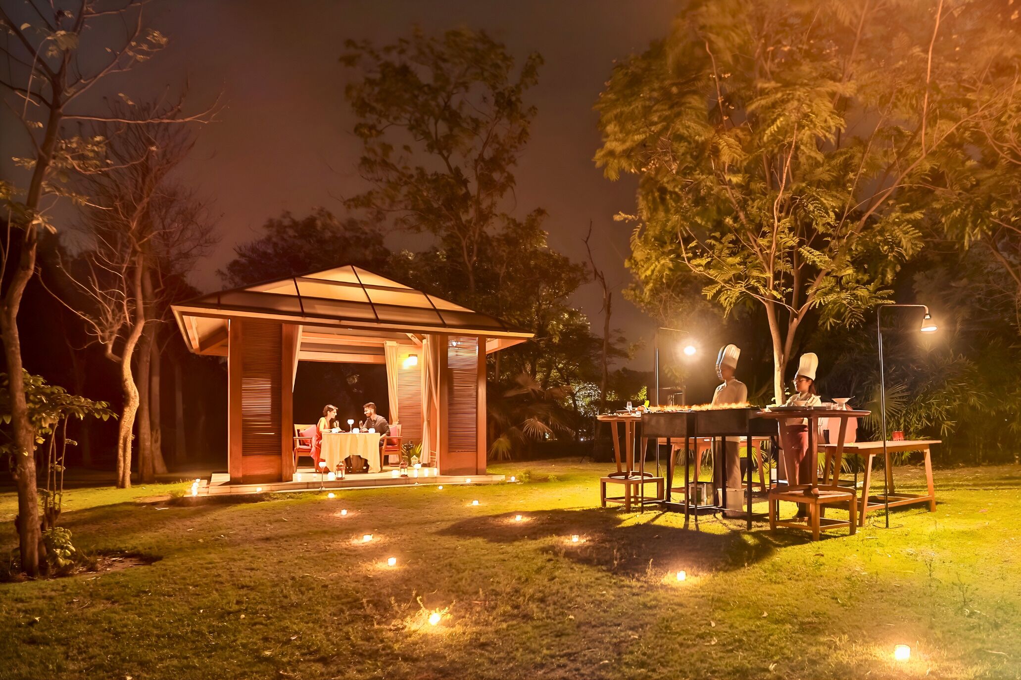 Un espace de restauration extérieur agréable, avec une table et des chaises, entouré d’arbres et d’un petit bâtiment dont la porte est ouverte.