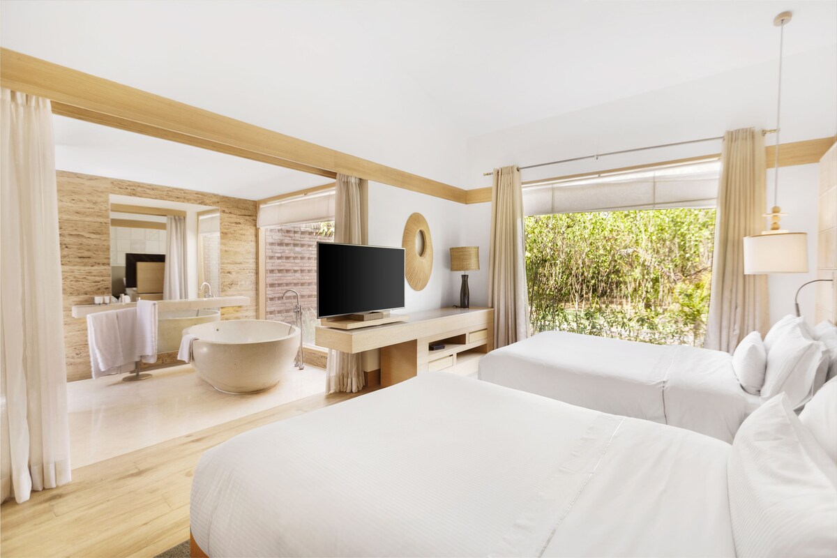 Habitación de hotel moderna con una cama grande, televisión, bañera y vistas a zonas verdes.