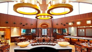 A spacious restaurant with multiple dining tables, a central bar area, and a distinctive circular chandelier. - The Westin Sohna Resort & Spa (Sohna)